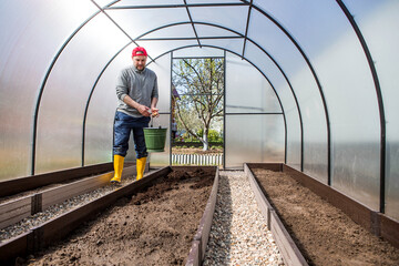 A male farmer pours new soil, soil for a new greenhouse. The concept of spring vegetable planting,...