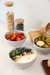 granola yogurt blueberry with salad tomato and bread in white ceramic bolw, isolated on white background.