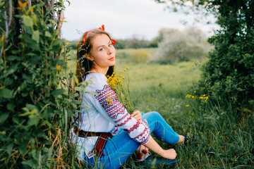 Woman in Traditional Embroidered Blouse Posing Outdoors Amid Greenery and Flowers