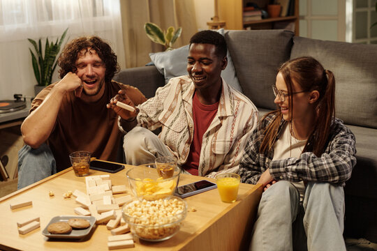 Intercultural friends laughing at broken wooden tower after African American guy removed block