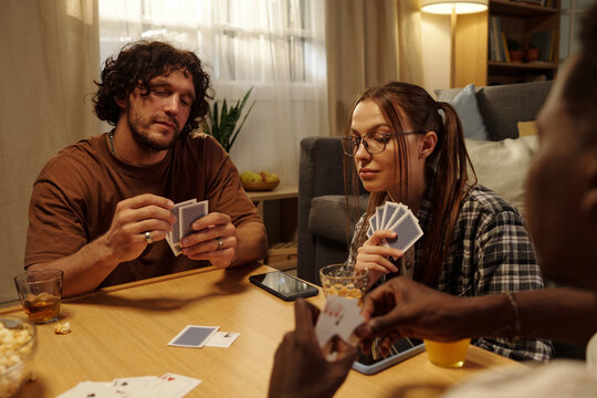 Group of young friends looking at their playing cards during tabletop game in home environment