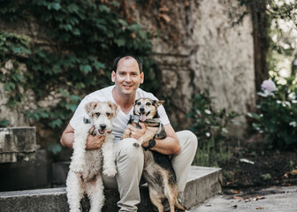 Portrait of a man in a park with his two dogs looking at the camera. Latin man smiles at camera, caring love for his pets.