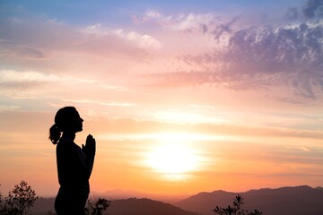 Obraz premium A silhouette of a woman standing with her hands clasped in a prayer or meditative pose