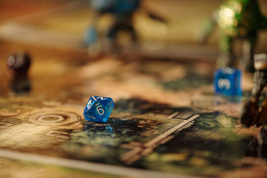 Blue cube dice with numbers lying on board game pictures included into tabletop entertainment stuff