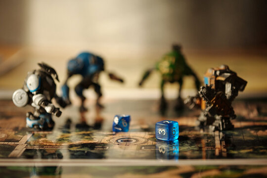 Two blue cube dices with numbers lying on tabletop game picture against several figurines of toy warriors - Powered by Adobe