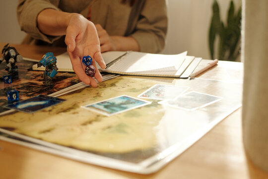 Hand of girl throwing dice cubes on picture of board game with cards while playing with friends by table