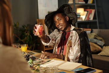 Happy young African American male participant of board game in costume showing card with his character