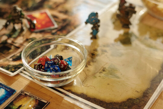 Transparent glass bowl with pile of colorful dice cubes with numbers standing on board game picture