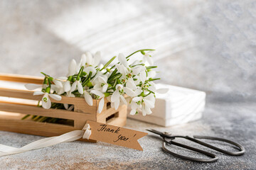 Fresh snowdrop flowers in a wooden box with a thank you tag