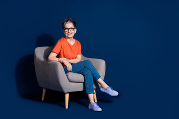 Full length photo of lovely pensioner lady sit armchair relaxed dressed stylish orange garment...