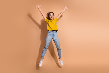 Excited young woman in casual outfit jumping with joy against beige background in studio