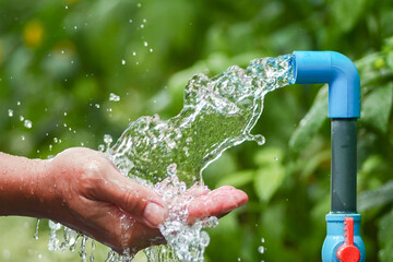 Refreshing Flow of Clean Water from a Blue Faucet onto Hands in a Lush Green Garden Setting