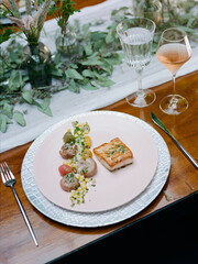 Elegant dining arrangement featuring beautifully plated dish with wine and decorative greenery at a sophisticated gathering