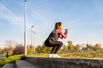 Fitness woman performing jump exercise in city park.