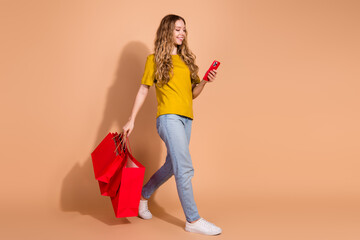 Cheerful young woman with red shopping bags and smartphone on beige background expressing joy of modern lifestyle and online shopping