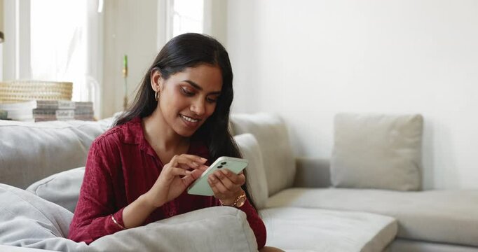 Woman resting on couch with smartphone, browsing, interacting on social media platform, playing immersive games on app stores, surfing web for news, blogs, and other amusing content. Modern tech usage