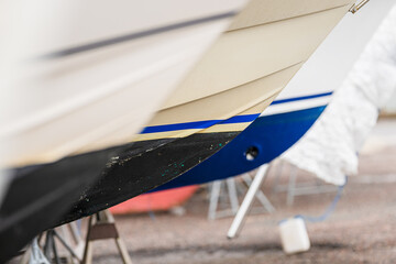 hulls of boats on stands in boatyard showing various paint schemes.