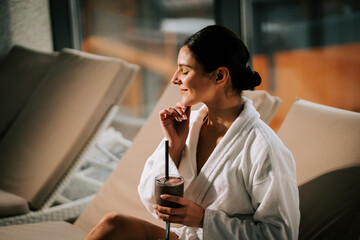 Woman in white robe enjoying a cocktail while relaxing in a spa setting with serenity and tranquility in the air