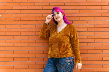 Body positive autistic woman with pink hair and glasses posing against brick wall