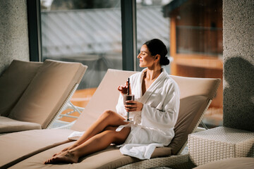 Woman in a white robe enjoys a refreshing cocktail while relaxing at a spa during a serene afternoon