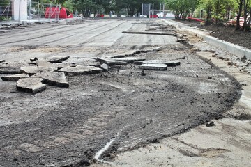 Freshly excavated section of asphalt road reveals the underlying dirt and gravel. The broken...