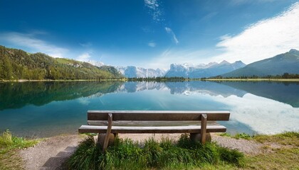 Obraz premium serene lake view with a wooden bench and mountains reflecting in the water under a bright sky