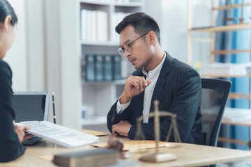 Law Consultation: A lawyer attentively listens to his client, reviewing documents on the table,...