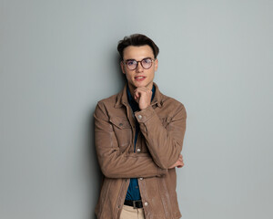 thoughtful young man with glasses touching chin and thinking