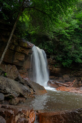 Obraz premium A serene waterfall cascades down rocks surrounded by lush greenery, creating a tranquil scene in a forest setting.