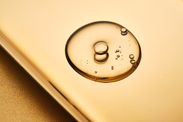 A beautiful drop of gel-like cosmetic serum with bubbles on a golden background.