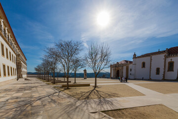 A spacious square with bare trees casting long shadows stretches towards historic buildings under a...