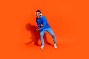 Young man enjoying music, dancing in a stylish outfit against orange background