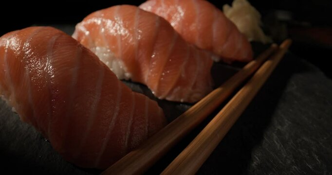 delicious Japanese food, pink salmon nigiri sushi rich in omega 3 fatty acids served perfectly with pickled ginger and wooden chopsticks on black background in a closeup video