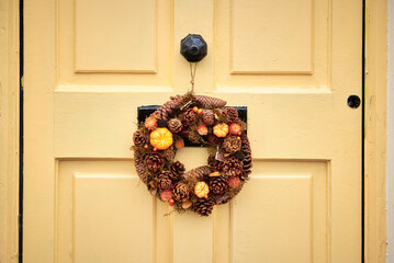 An elegant autumn wreath featuring pinecones, orange accents, and dried foliage adorning a charming yellow door in Cobh, Ireland, showcasing seasonal decoration and a warm aesthetic © EvaMara