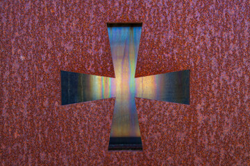 A metallic cross with a textured, iridescent surface is centrally framed against a dark, rough...