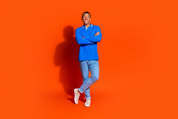 Stylish young man in blue shirt posing against vibrant orange background