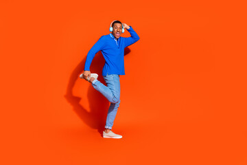 Joyful young man in blue polo poses against vibrant orange background