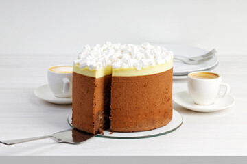 A chocolate homemade pie decorated with a marshmallow and two cups of coffee on a white wooden table. Shallow focus