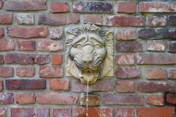A drinking fountain shaped like a lion's head, built into a brick wall.
