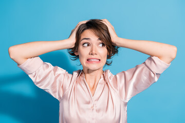 Fototapeta premium Young businesswoman in stylish pink shirt expresses funny surprise with hands on head against blue background