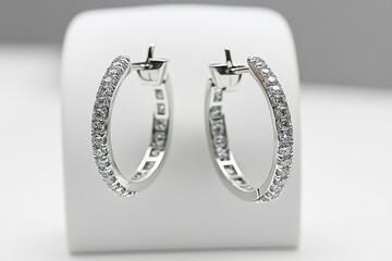 Modern white gold hoop earrings encrusted with diamonds displayed on a minimalist jewelry stand