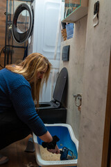 Cleaning a litter box in a laundry room during the evening