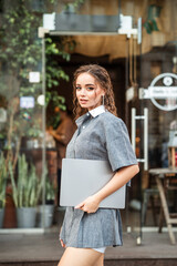 A young girl is holding a laptop and smiling on the street.
