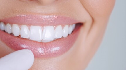Fototapeta premium Close up of a woman's bright, white smile with pink lips and a hint of lip gloss. A gloved hand is gently touching her lower lip. Neutral background.