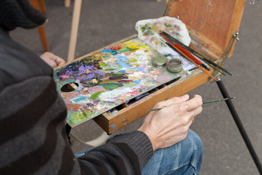Rear view of a street artist painting a cityscape while sitting at an easel.
