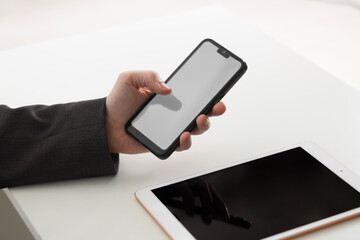 Businessman using smartphone near tablet at white table indoors, closeup. Modern technology