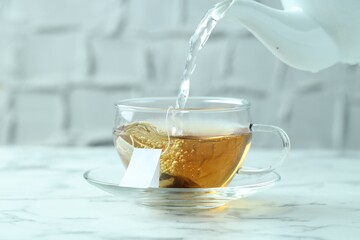 Pouring hot water into cup with tea bag on light marble table, closeup