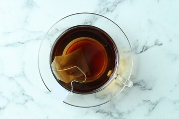 Tea bag in glass cup with hot drink on light marble table, top view