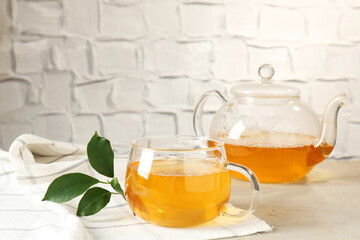 Refreshing green tea and leaves on light table against textured wall, closeup
