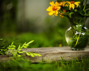 yellow and orange flowers in a glass vase on a wooden stand in tall green grass in a summer garden, space for a subject, summer composition, spring garden, fragrant flowers